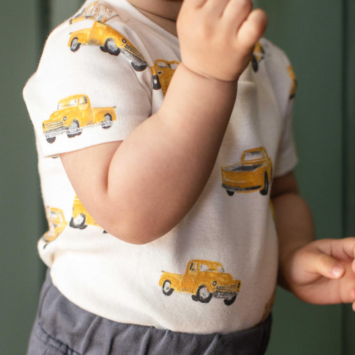Baby wearing white short-sleeve tee with yellow vintage truck print and gray shorts