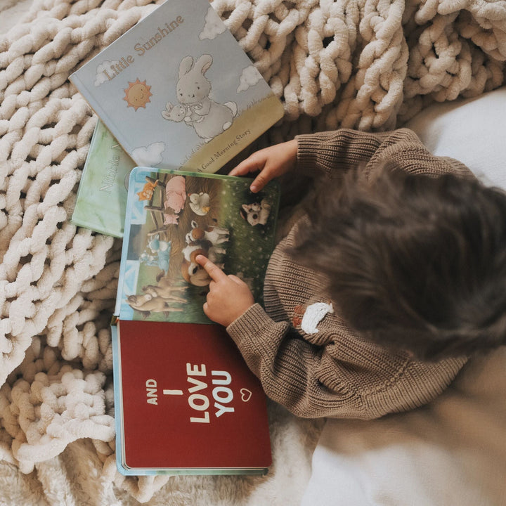 Child reading Bunnies by the Bay 'You Are My Baby' board book collection on cozy blanket.