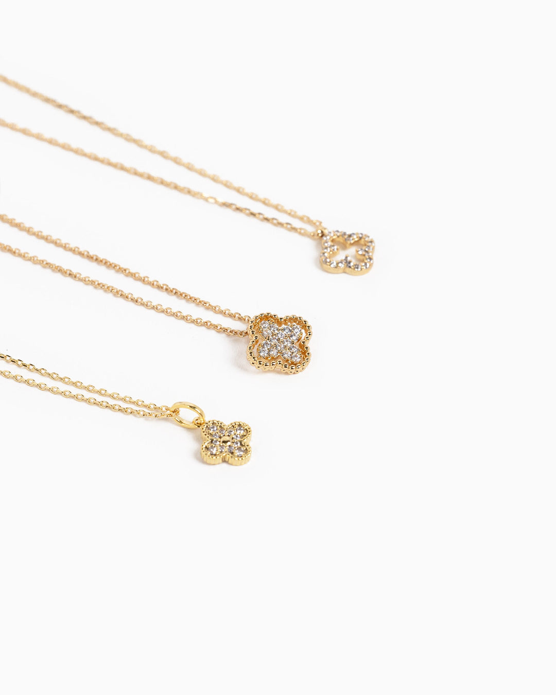 Three gold clover necklaces with CZ pavé stones displayed on white background, varying sizes.