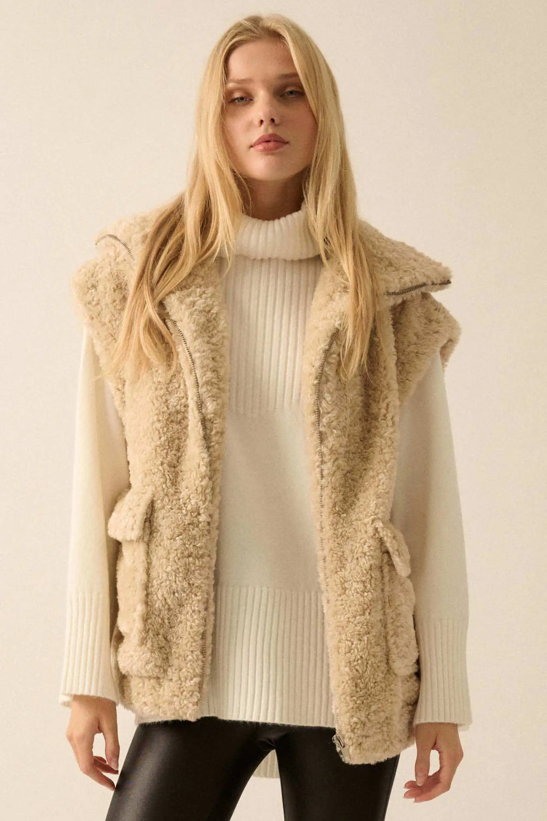 Woman wearing cream colored faux fur zip-up vest over white turtleneck sweater