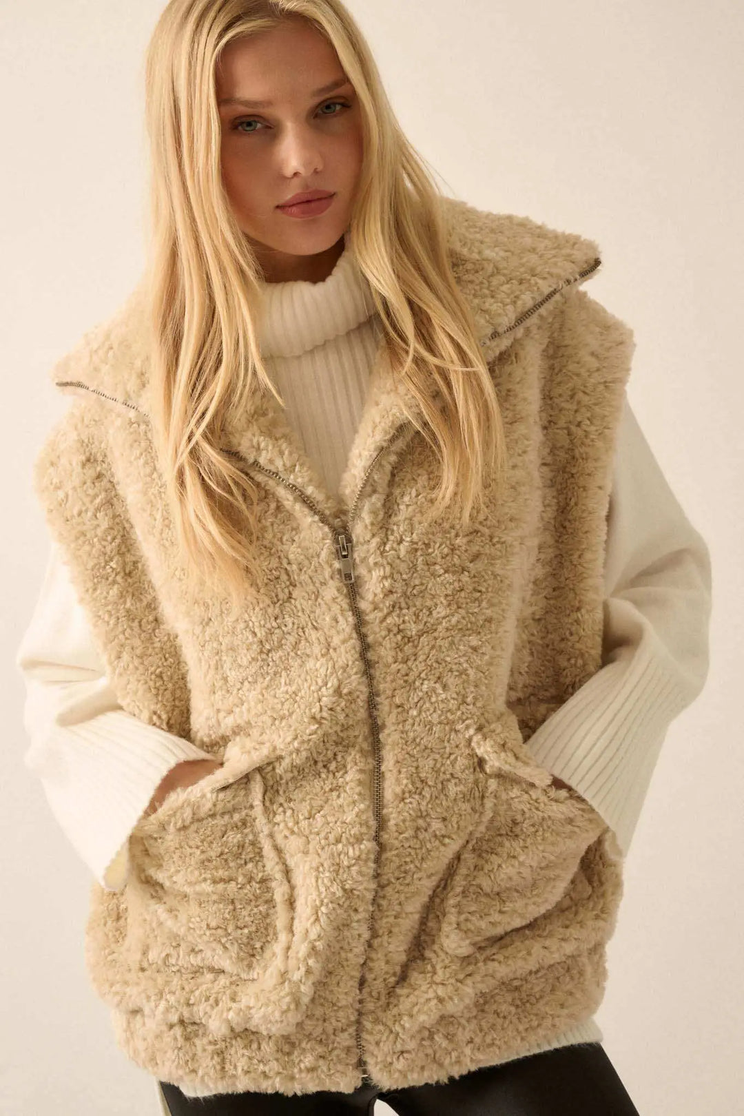 Woman wearing cream colored faux fur zip-up vest with white turtleneck sweater