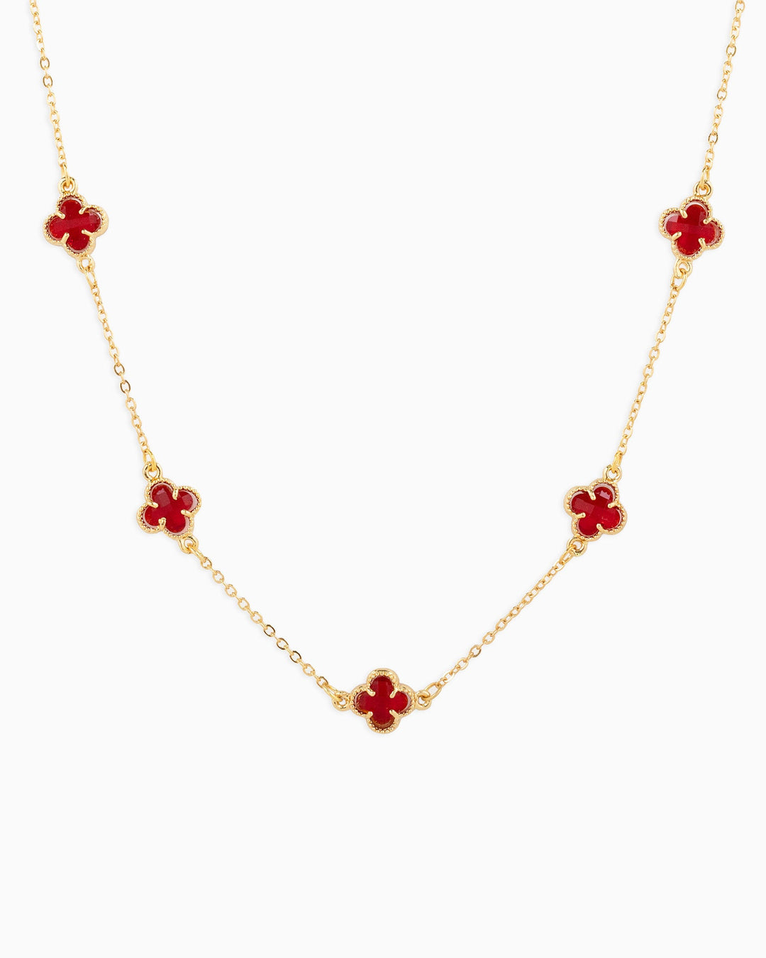 Gold station necklace featuring five red clover-shaped charms on a delicate chain.