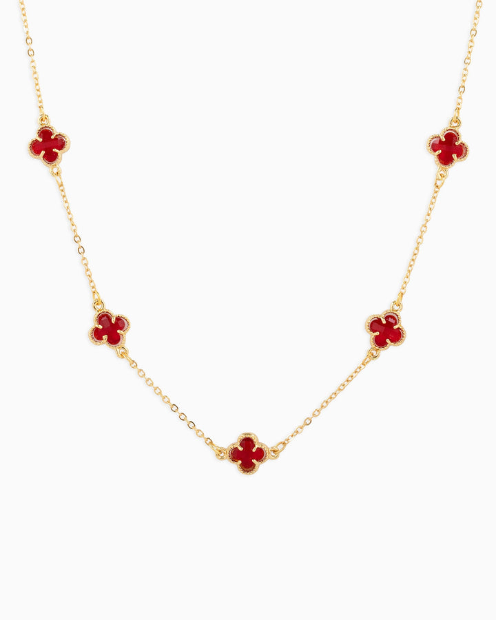 Gold station necklace featuring five red clover-shaped charms on a delicate chain.