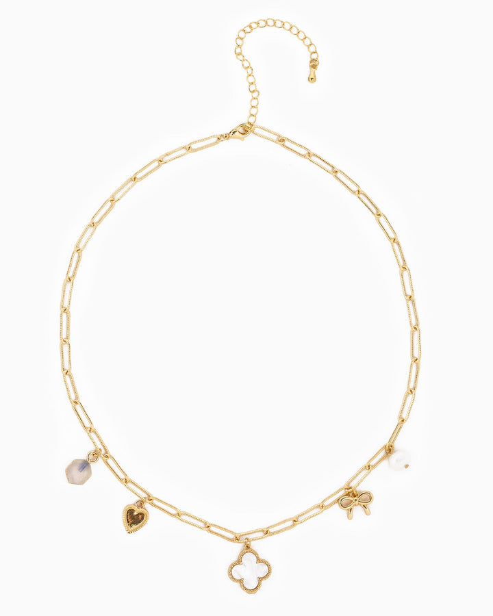 Gold paperclip chain necklace with clover, heart, bow, and crystal charms on white background.