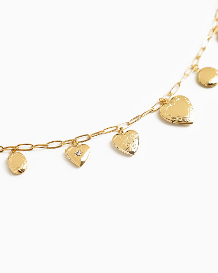 Gold chain necklace featuring seven heart-shaped locket charms with floral engravings and a crystal accent.