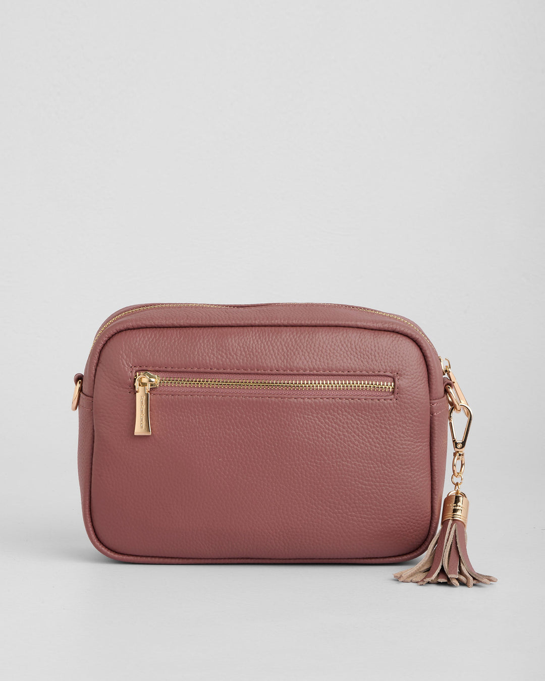 Dusty rose leather crossbody bag with gold hardware and tassel detail on white background