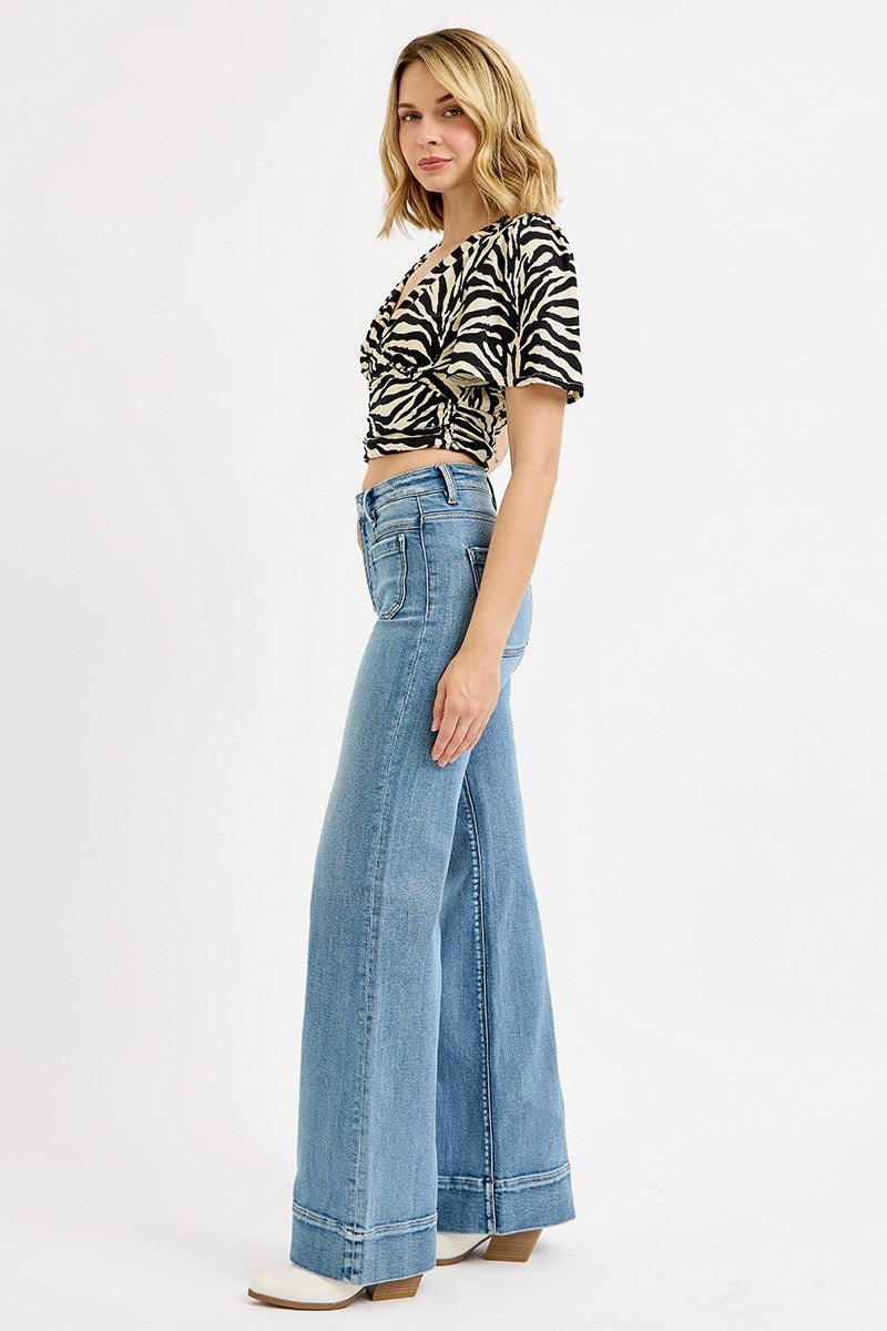 Woman wearing high rise wide flare jeans in medium wash denim with zebra print top