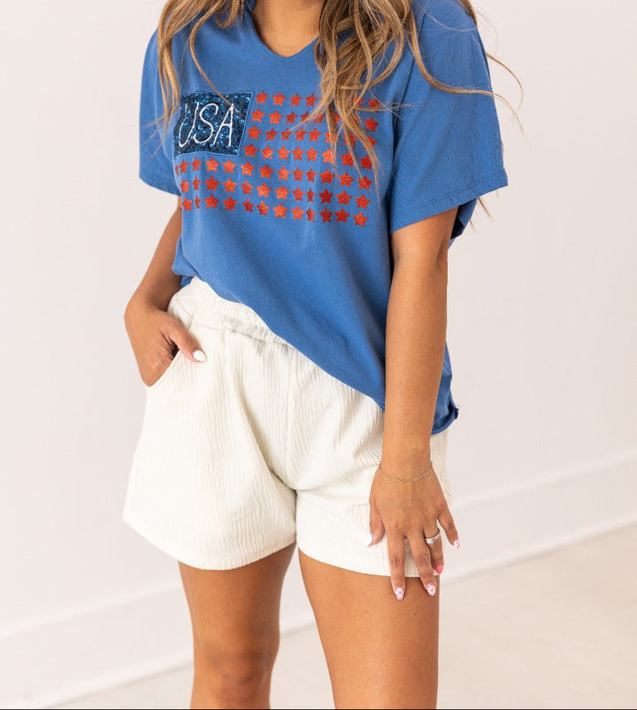 Woman wearing blue USA flag t-shirt with red glitter stars and white shorts