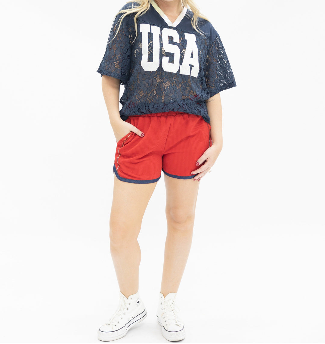 Woman wearing navy lace USA jersey top with red shorts and white sneakers