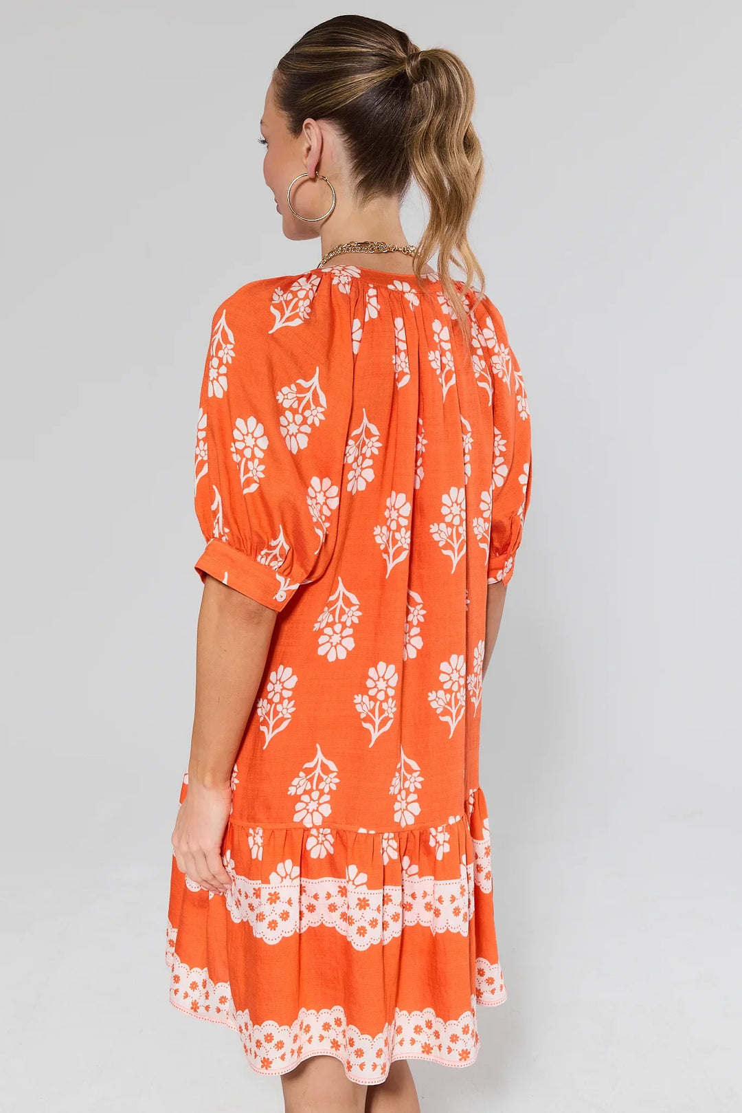 Orange floral dress with white flower print, three-quarter sleeves, and ruffled hem detail