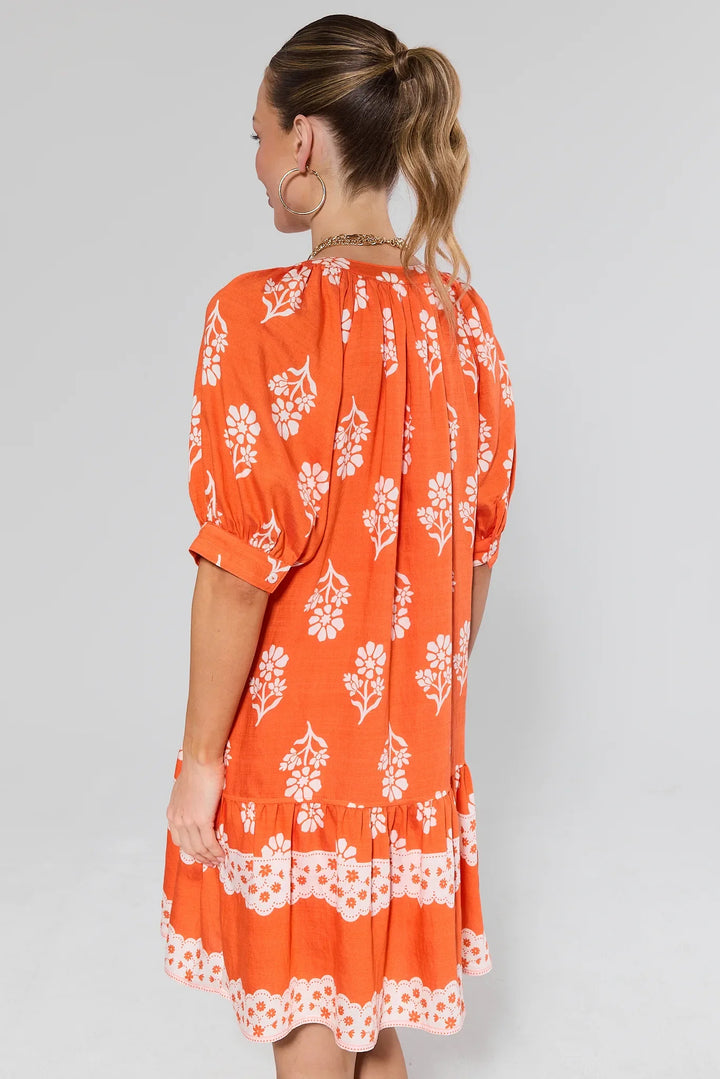 Orange floral dress with white flower print, three-quarter sleeves, and ruffled hem detail