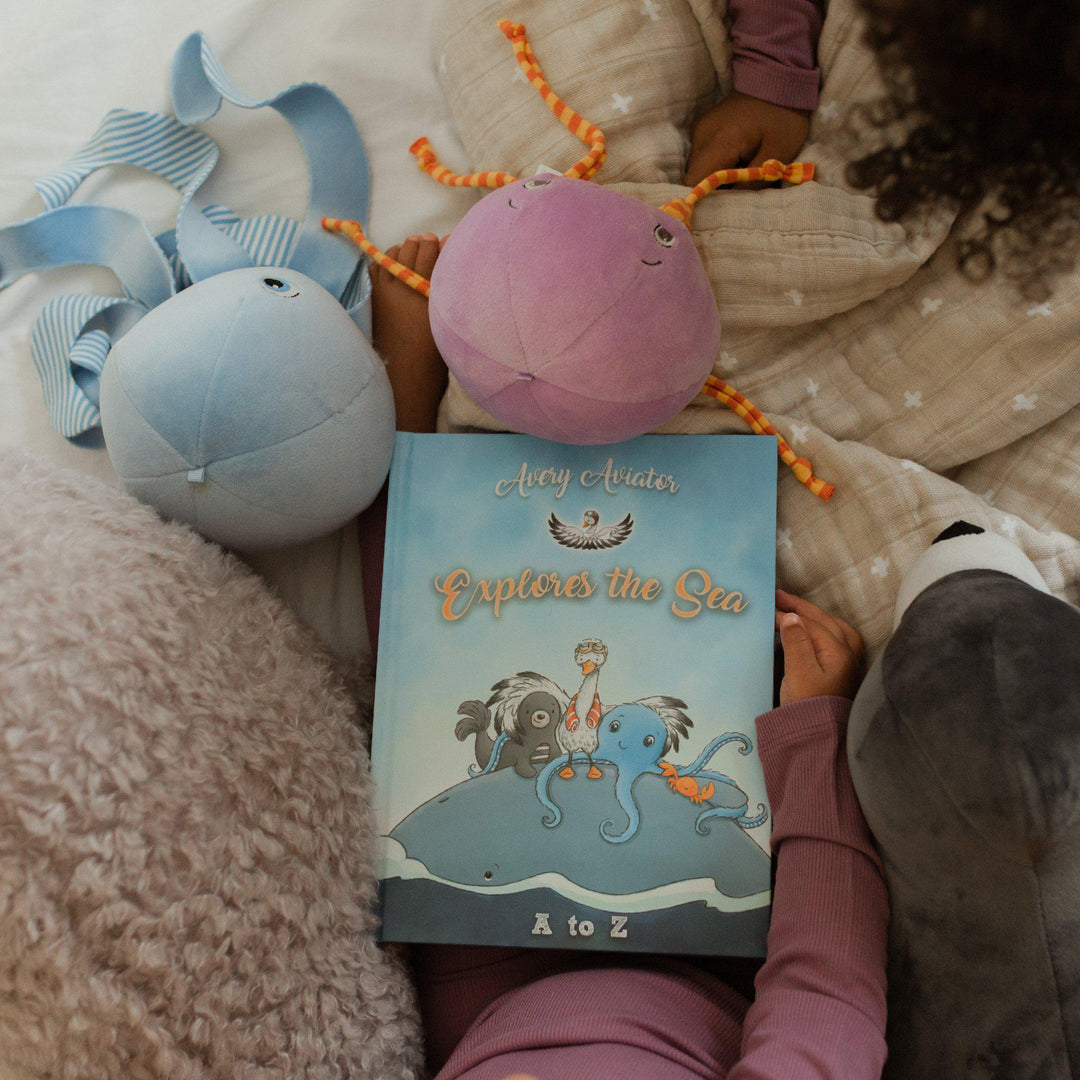 Child holding Avery Aviator Explores the Sea A to Z children's book with plush toys nearby