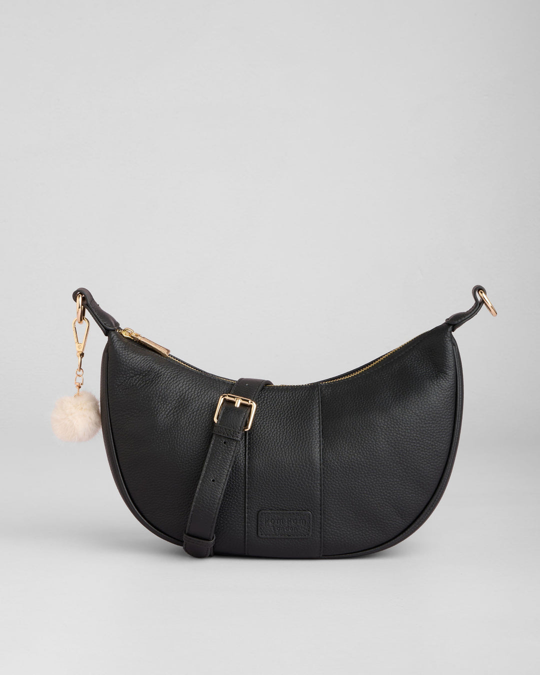 Black Pom Pom London Sutton Sling Bag with cream pom pom charm on white background