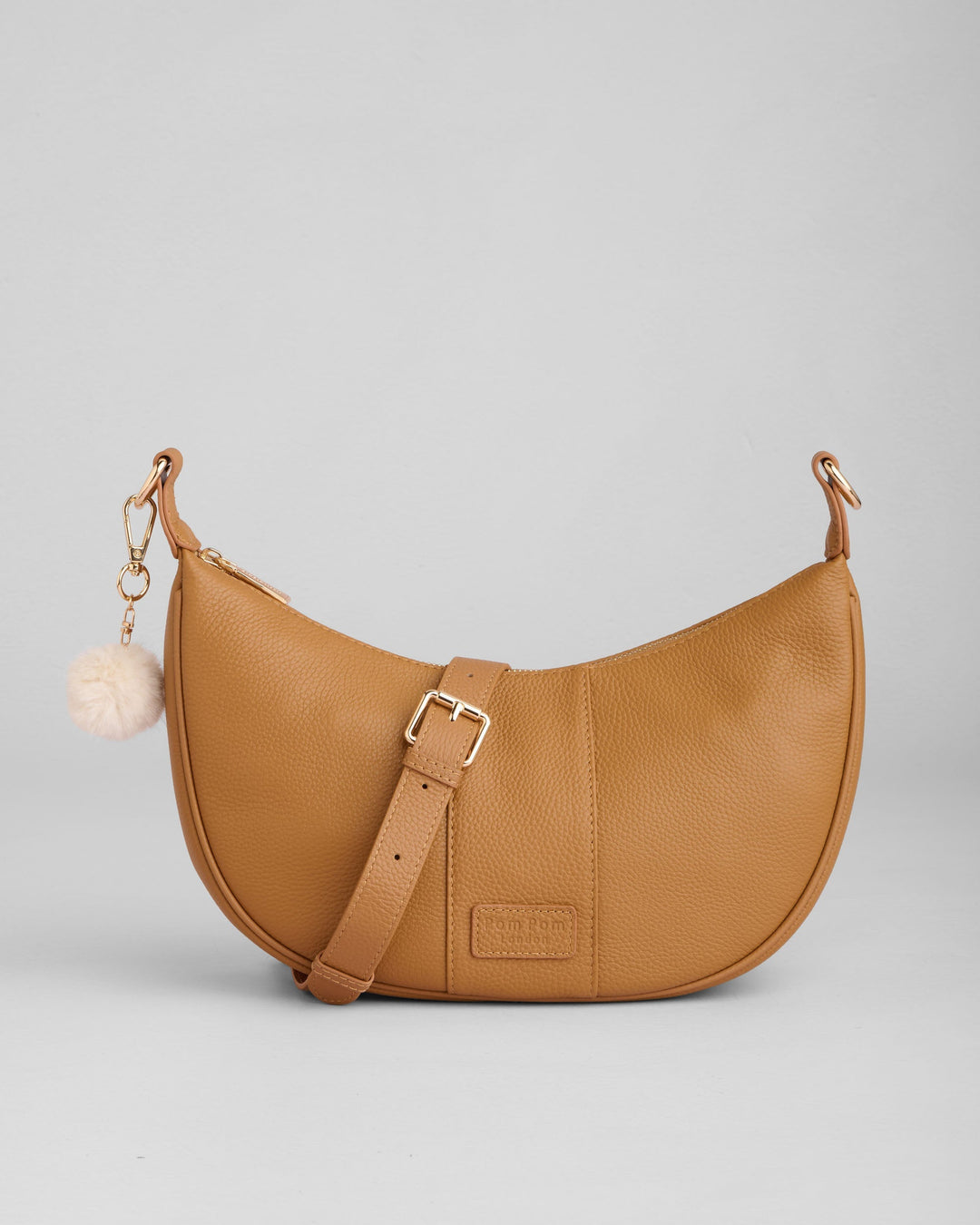 Tan leather Sutton Sling Bag with crossbody strap and white pom pom charm