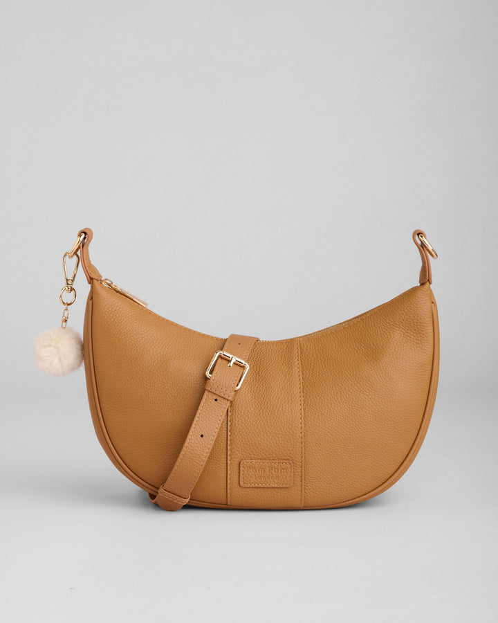 Tan leather Sutton Sling Bag with crossbody strap and white pom pom charm