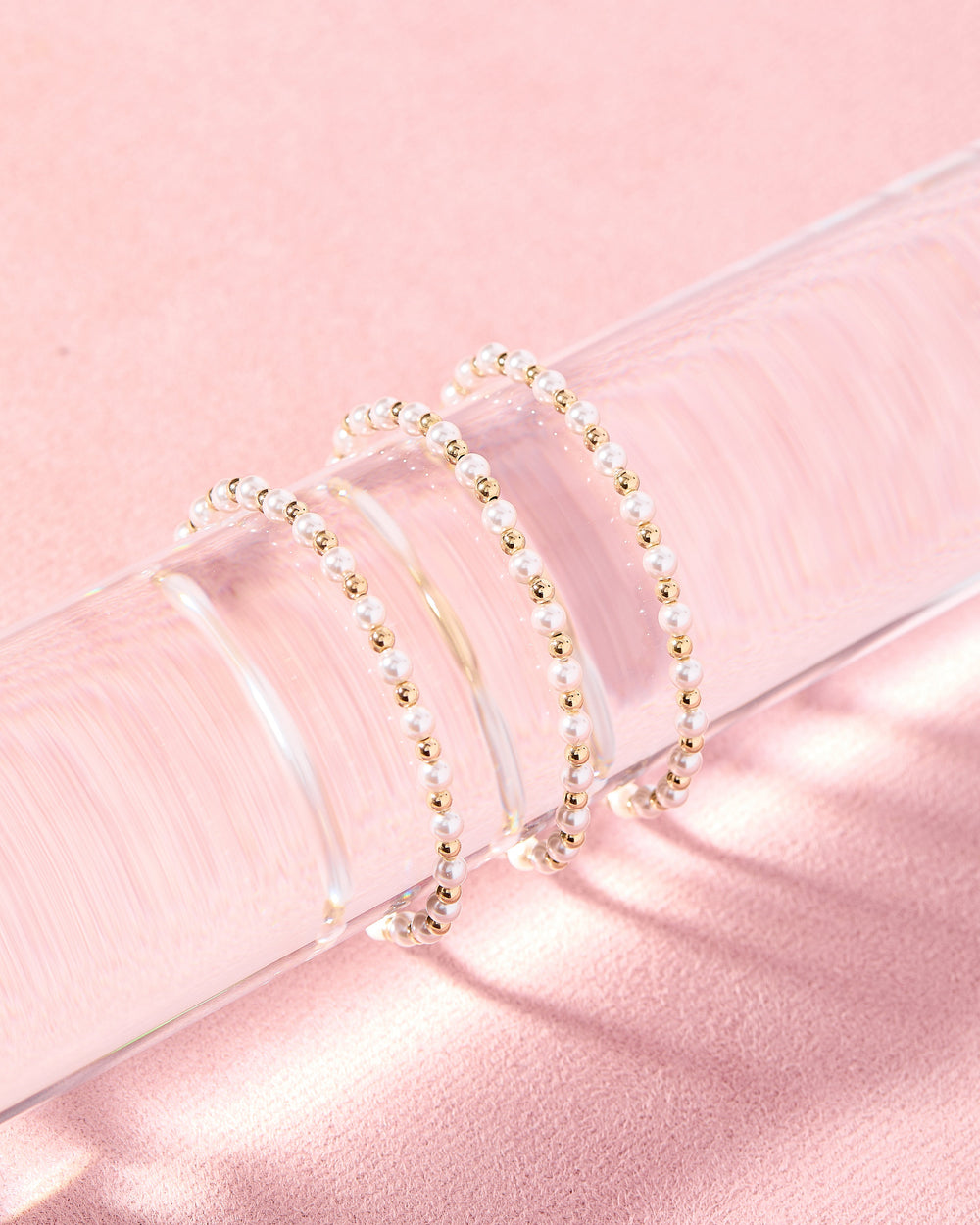 Three Luci Pearl and gold beaded stretch bracelets displayed on a clear acrylic stand