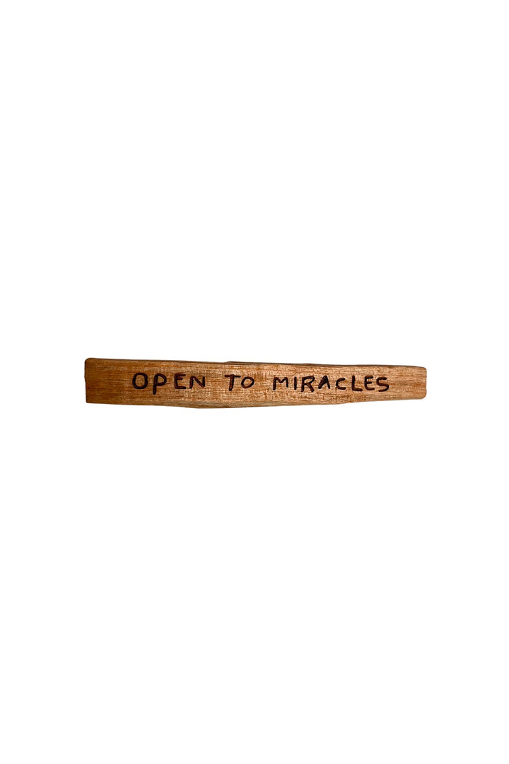 A single palo santo stick with 'Open To Miracles' mantra burned into the wood.