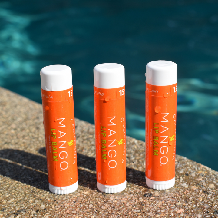 Three California Mango lip balm sticks with SPF 15 and beeswax beside a pool.