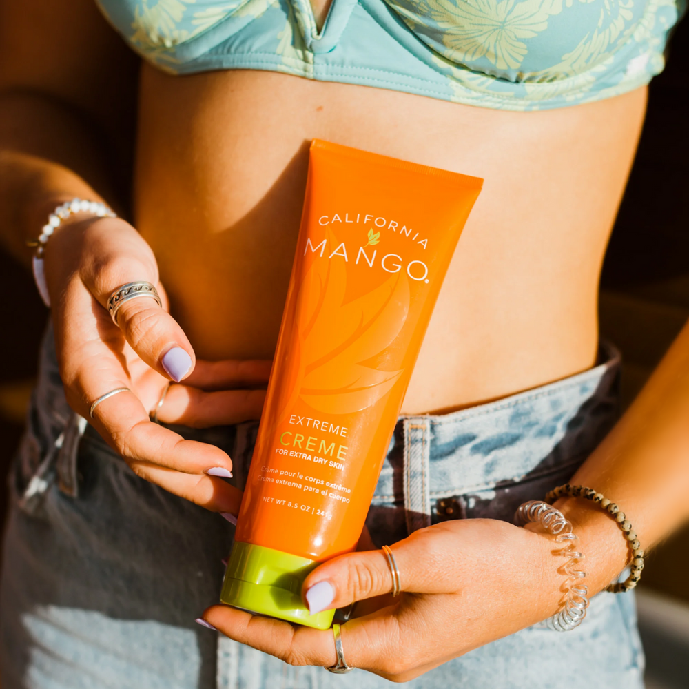 California Mango Extreme Creme 8.5oz orange tube held by hands with jewelry