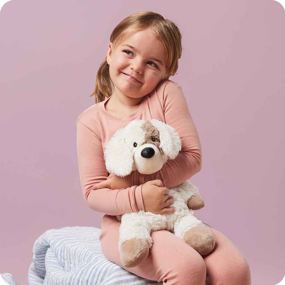Young girl hugging Warmies stuffed puppy toy with cream fur and brown spots