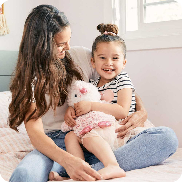 Mother and child cuddling with pink Warmies plush penguin on bed