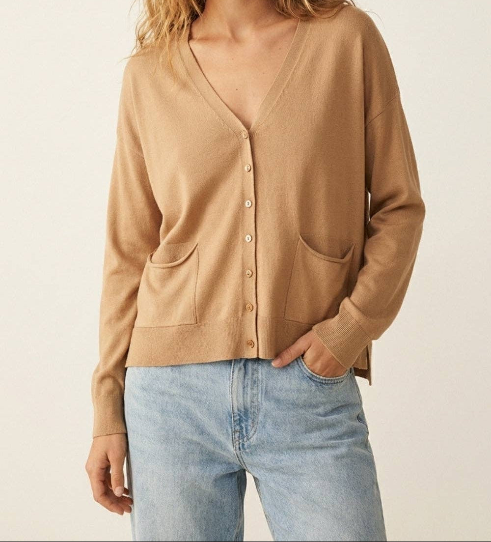 Woman wearing camel colored fine knit cardigan with buttons and pockets over light blue jeans