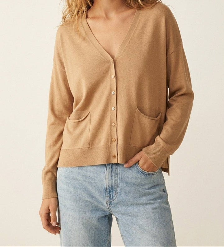 Woman wearing camel colored fine knit cardigan with buttons and pockets over light blue jeans