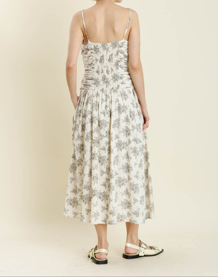 Woman wearing ivory floral midi dress with shirred bodice and thin straps, back view