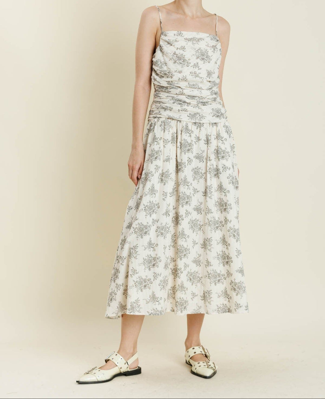 Woman wearing ivory midi dress with gray floral print, spaghetti straps, and shirred bodice