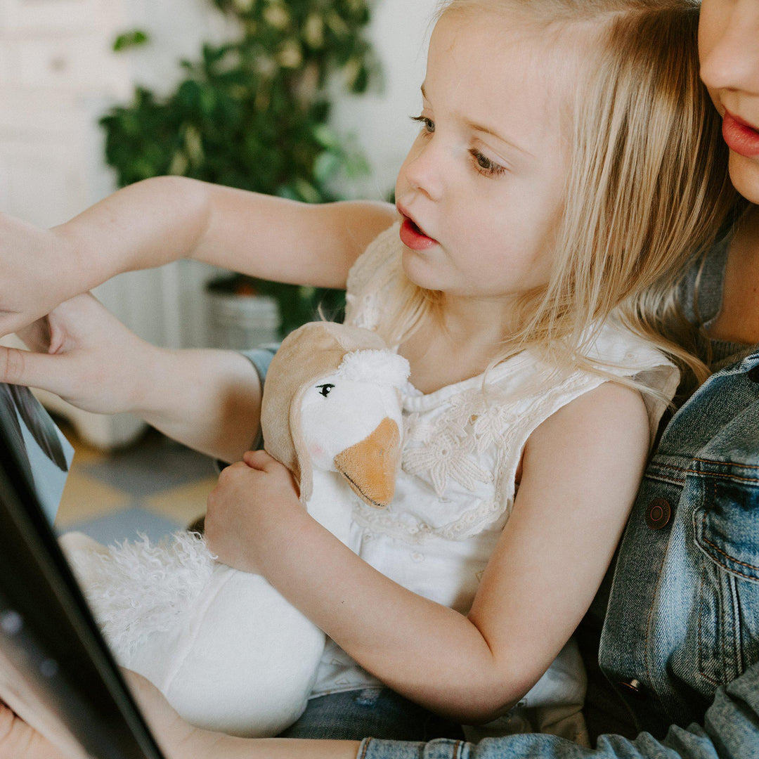 Child holding a white duck plush toy while reading Bunnies by the Bay Arctic storybook