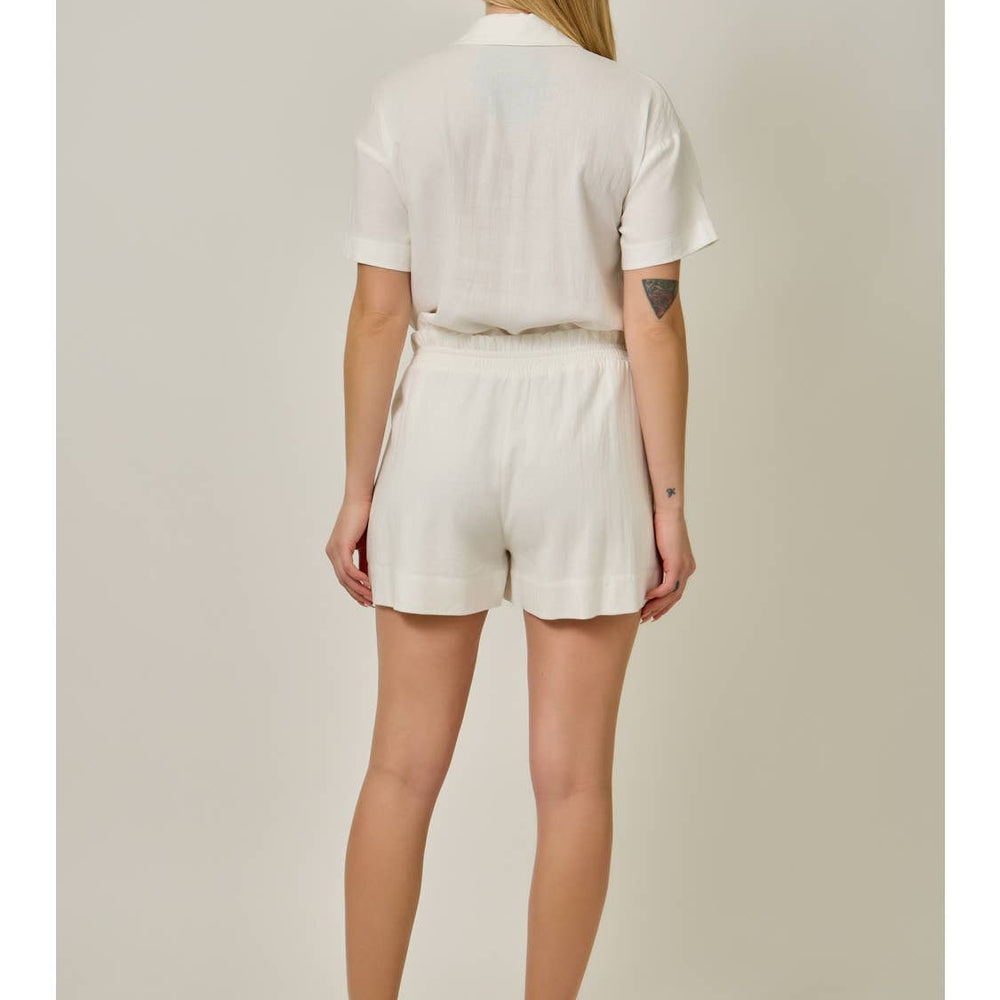 Woman wearing ivory linen shorts and matching top, back view studio photo