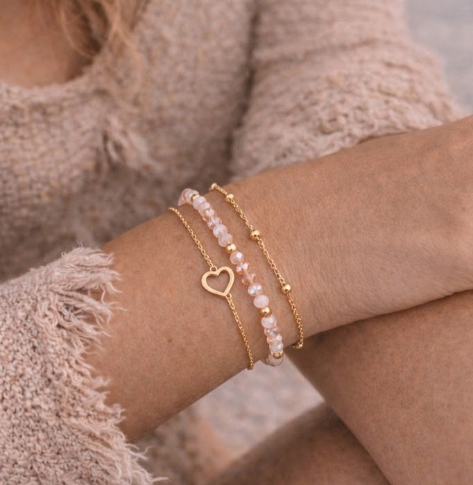 Set of three gold and rosy blush beaded bracelets with heart charm worn on wrist