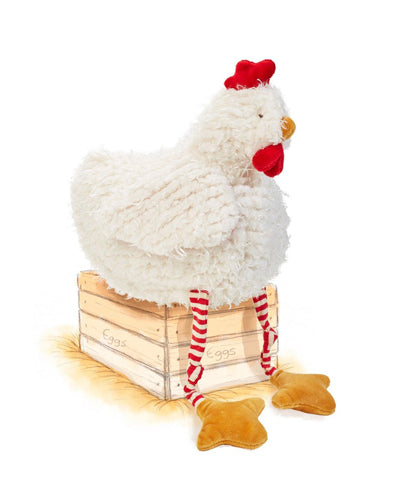 White fluffy plush chicken toy sitting on wooden crate with red striped ribbon