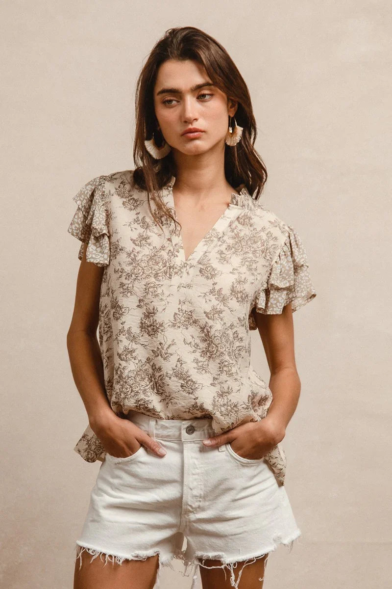 Woman wearing cream floral printed ruffled short sleeve top with white denim shorts
