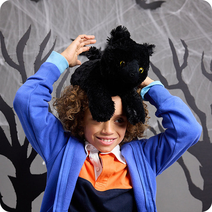 Child wearing black cat Warmies stuffed animal on head with yellow eyes