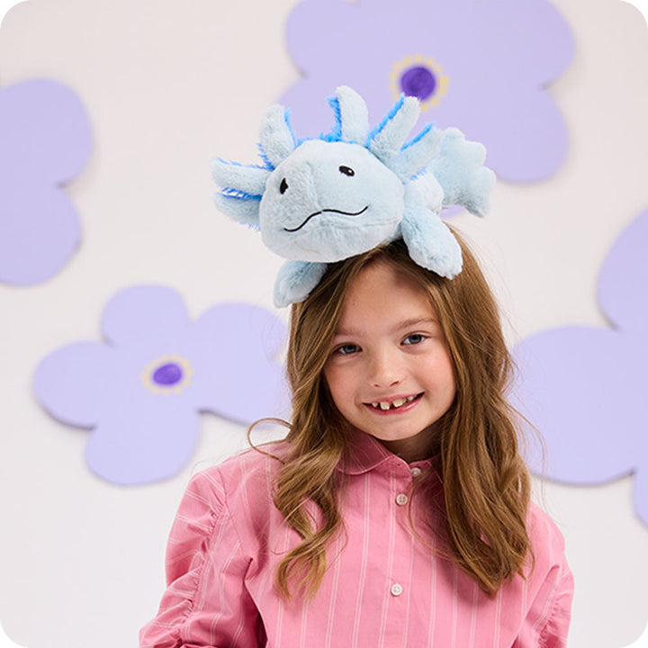 Young girl wearing light blue plush axolotl Warmies stuffed animal on her head, smiling