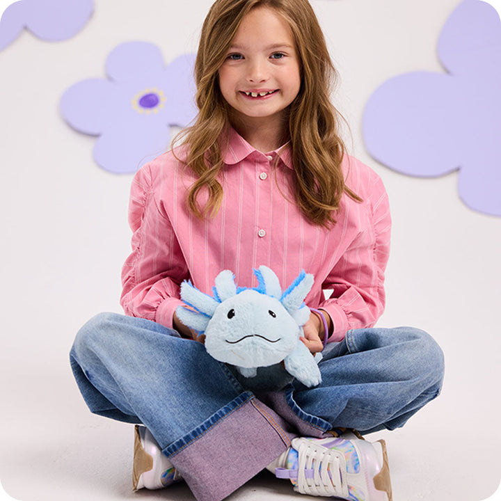 Child holding light blue Warmies axolotl plush toy with decorative flower background