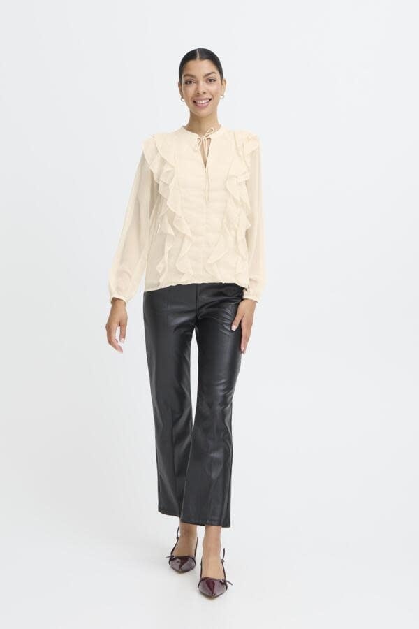 Woman wearing cream ruffled blouse with black leather pants in studio setting