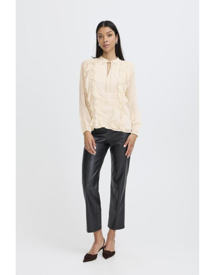 Woman wearing cream textured long-sleeve blouse with keyhole neckline and black leather pants