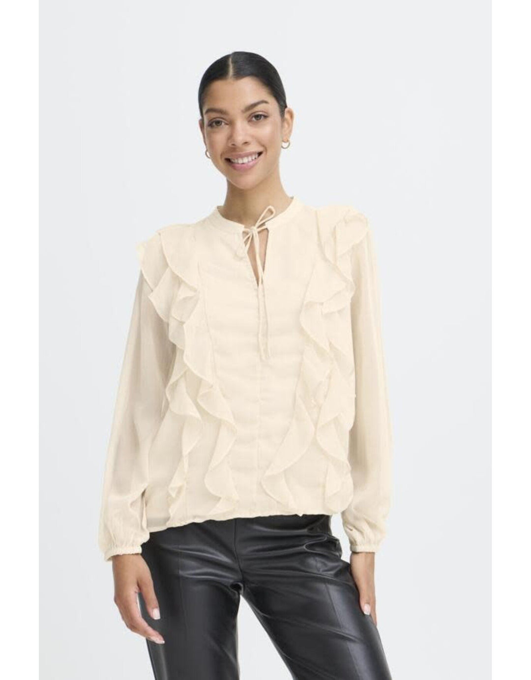 Woman wearing cream colored ruffled blouse with tie neck and black leather pants