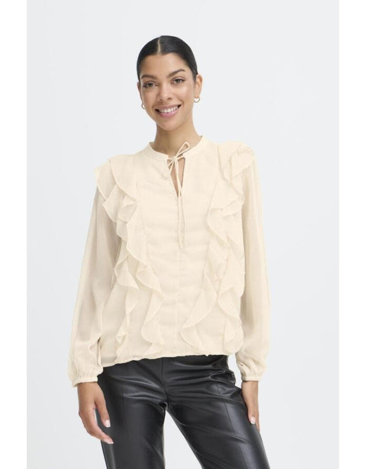 Woman wearing cream colored ruffled blouse with tie neck and black leather pants