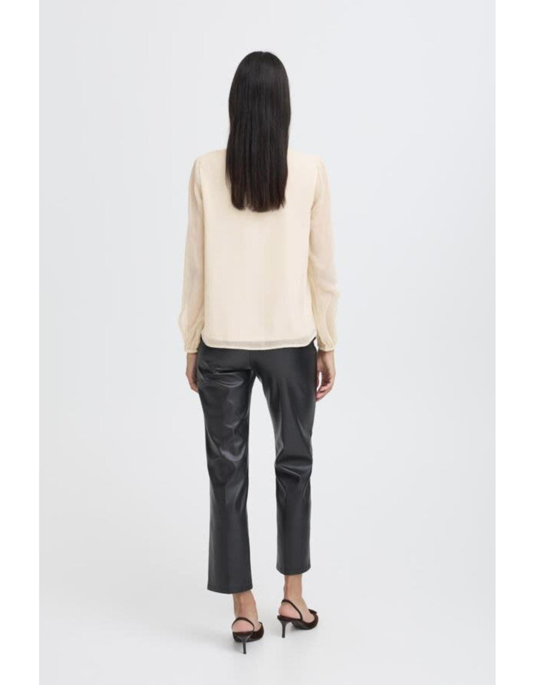 Woman wearing cream colored long-sleeve blouse with black leather pants, back view