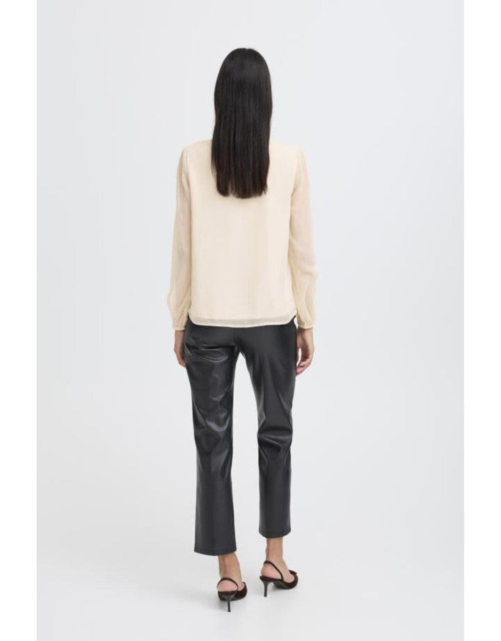Woman wearing cream colored long-sleeve blouse with black leather pants, back view
