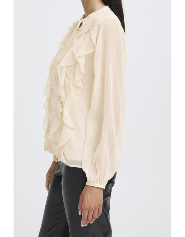 Woman wearing cream colored ruffled blouse with tie neck and long sleeves