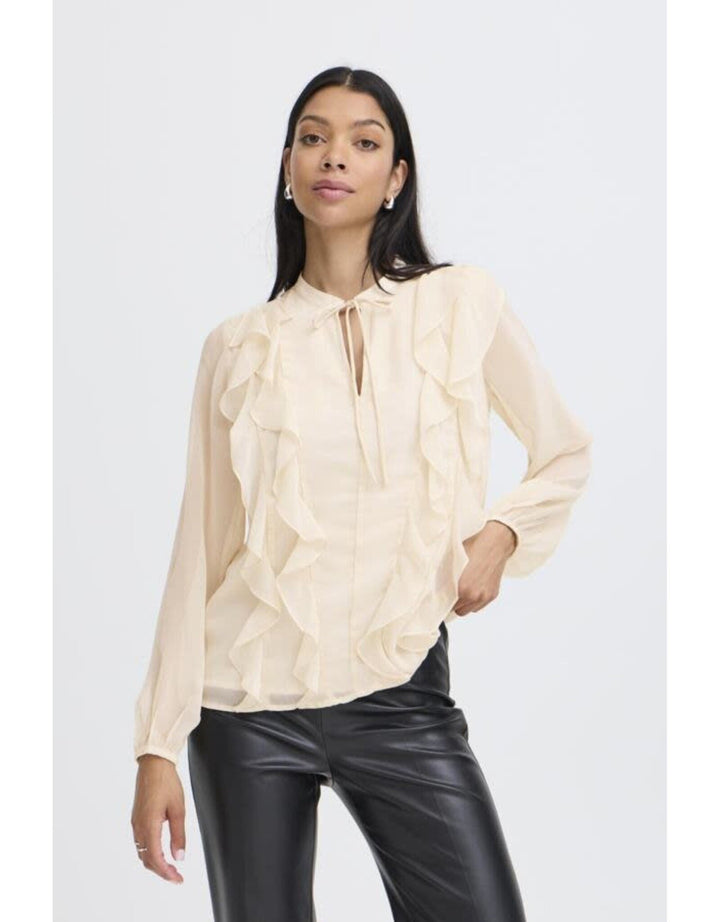 Woman wearing cream colored ruffled blouse with tie neck and black leather pants