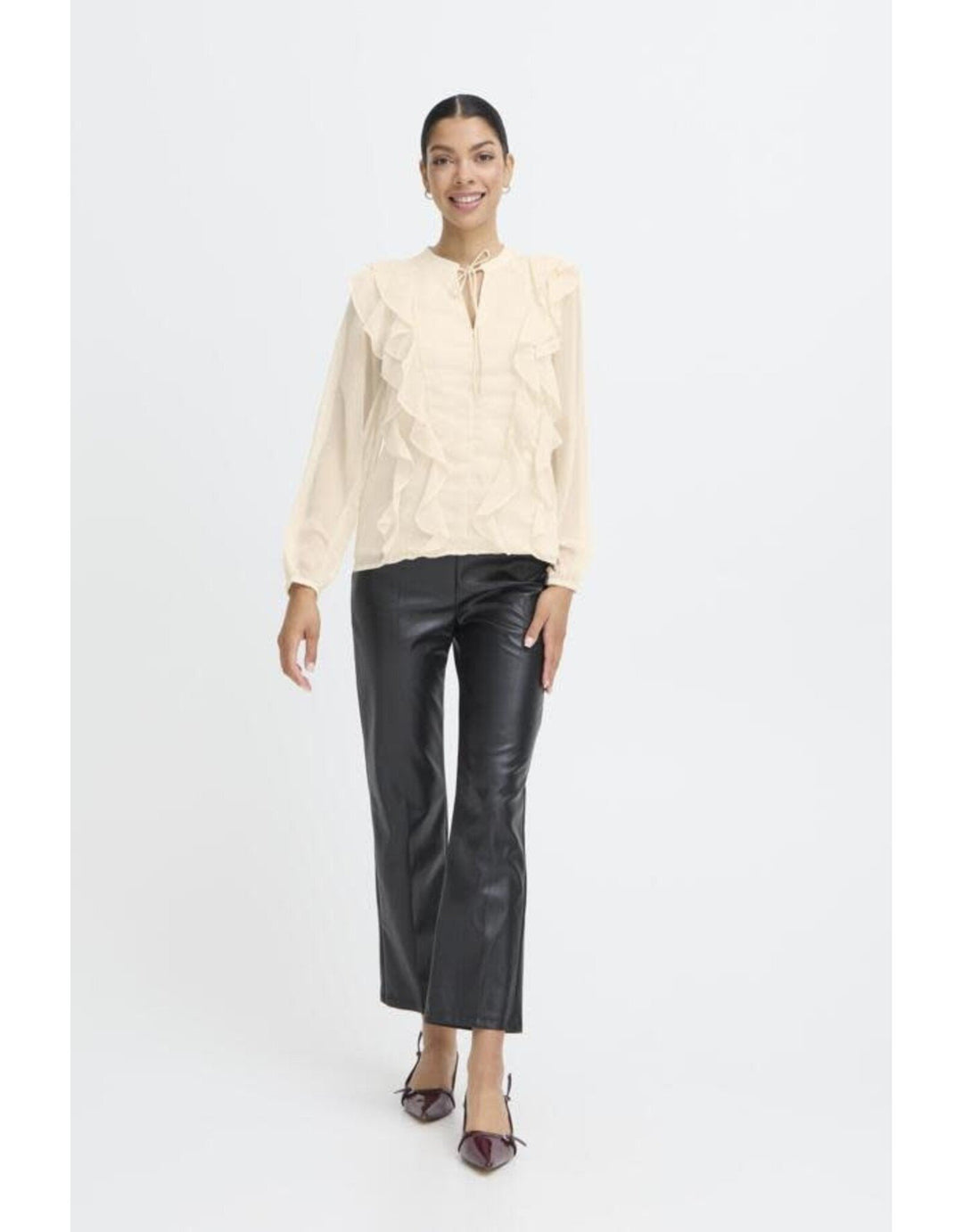Woman wearing cream frill blouse with tie neck and black leather pants