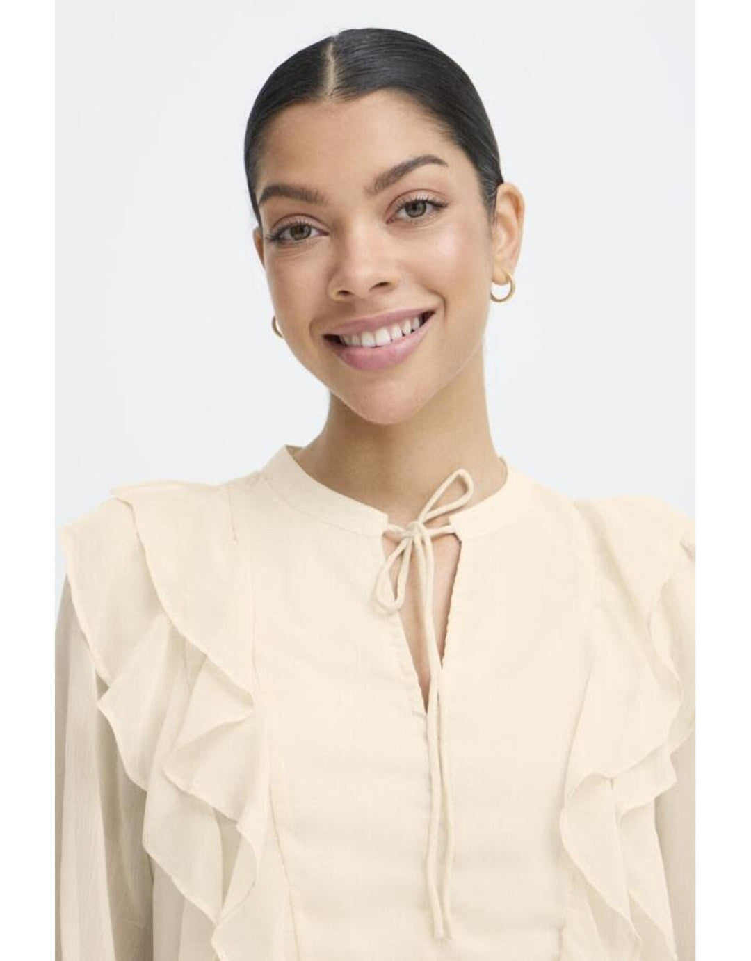 Woman wearing cream colored ruffled blouse with tie neck detail and long sleeves