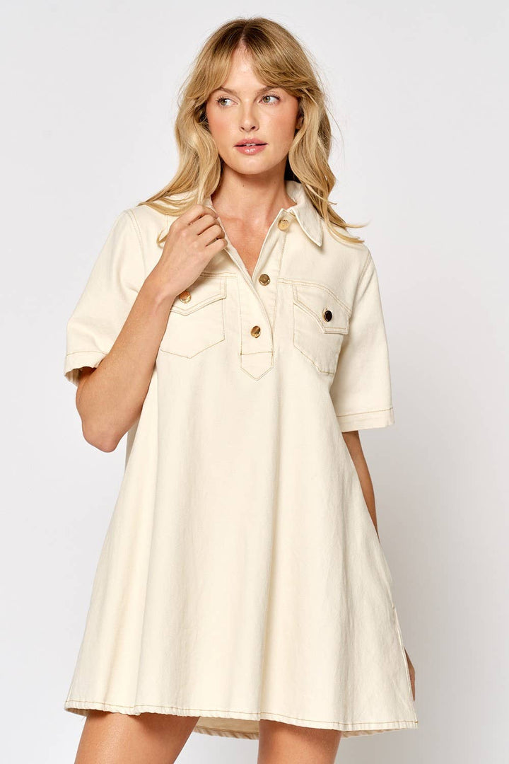 Woman wearing cream colored short sleeve button down shirt dress with collar and pockets