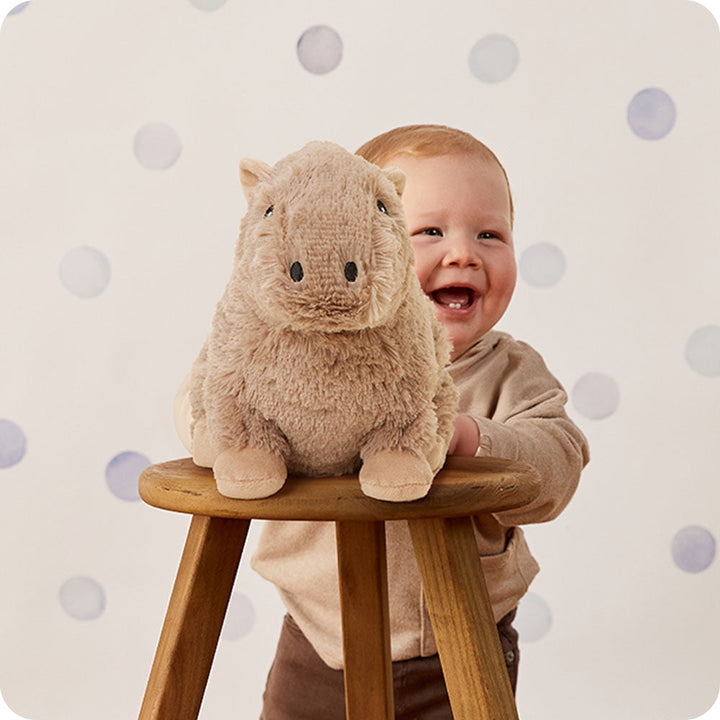 Warmies plush capybara toy in tan color with baby on wooden stool
