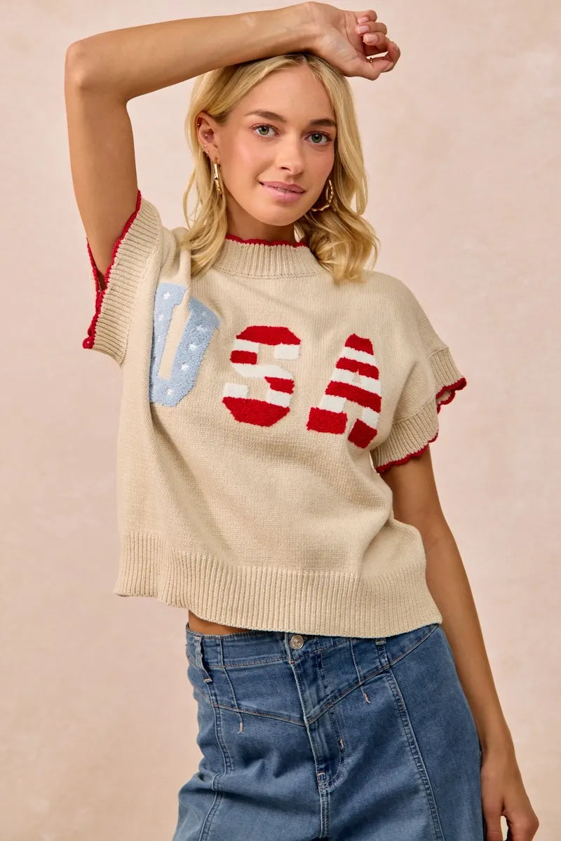 Woman wearing oatmeal colored sweater vest with red and blue USA patchwork lettering